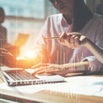Team working on a project in loft office. Two women discussing marketing plan. Laptop and paperwork on the table. Statistic graph overlay, icon innovation interface